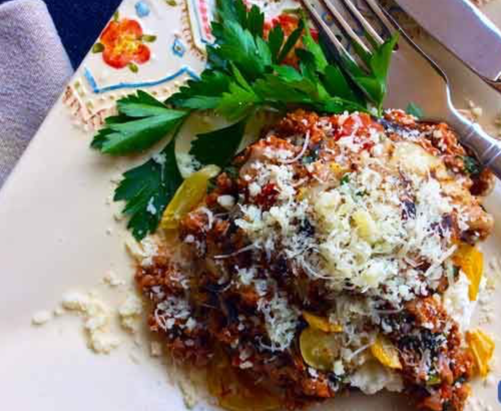 Plate of baked pasta or lasagna topped with tomato meat sauce, melted cheese, and parsley garnish.