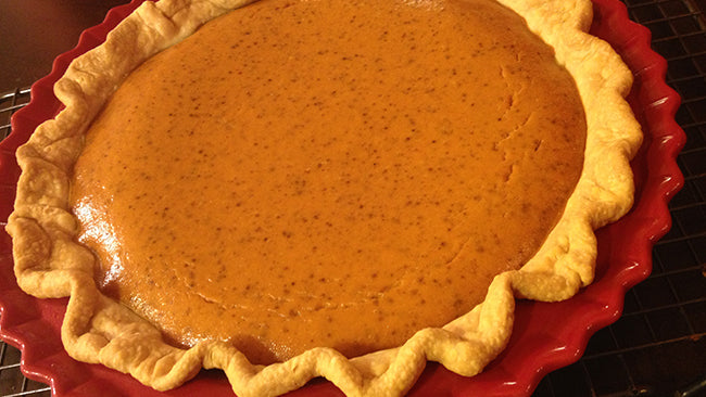 Freshly baked pumpkin pie with a golden, crimped crust in a red pie dish.