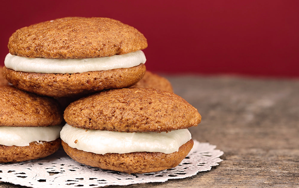Soft brown whoopie pies filled with creamy white frosting, stacked on a lace doily against a red background.