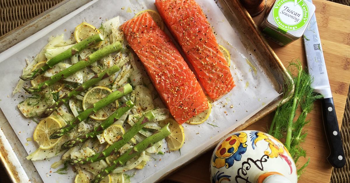 Salmon fillets on a sheet pan with asparagus, fennel, and lemon slices seasoned and ready to bake.