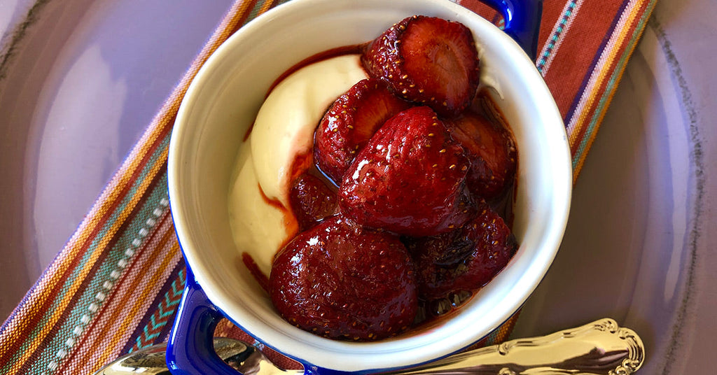 Bowl of yogurt topped with glazed strawberries in a small blue-handled dish.