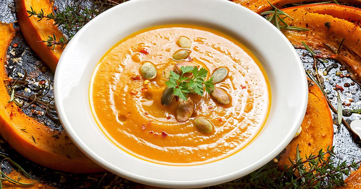 Creamy pumpkin soup topped with pumpkin seeds and herbs in a white bowl.