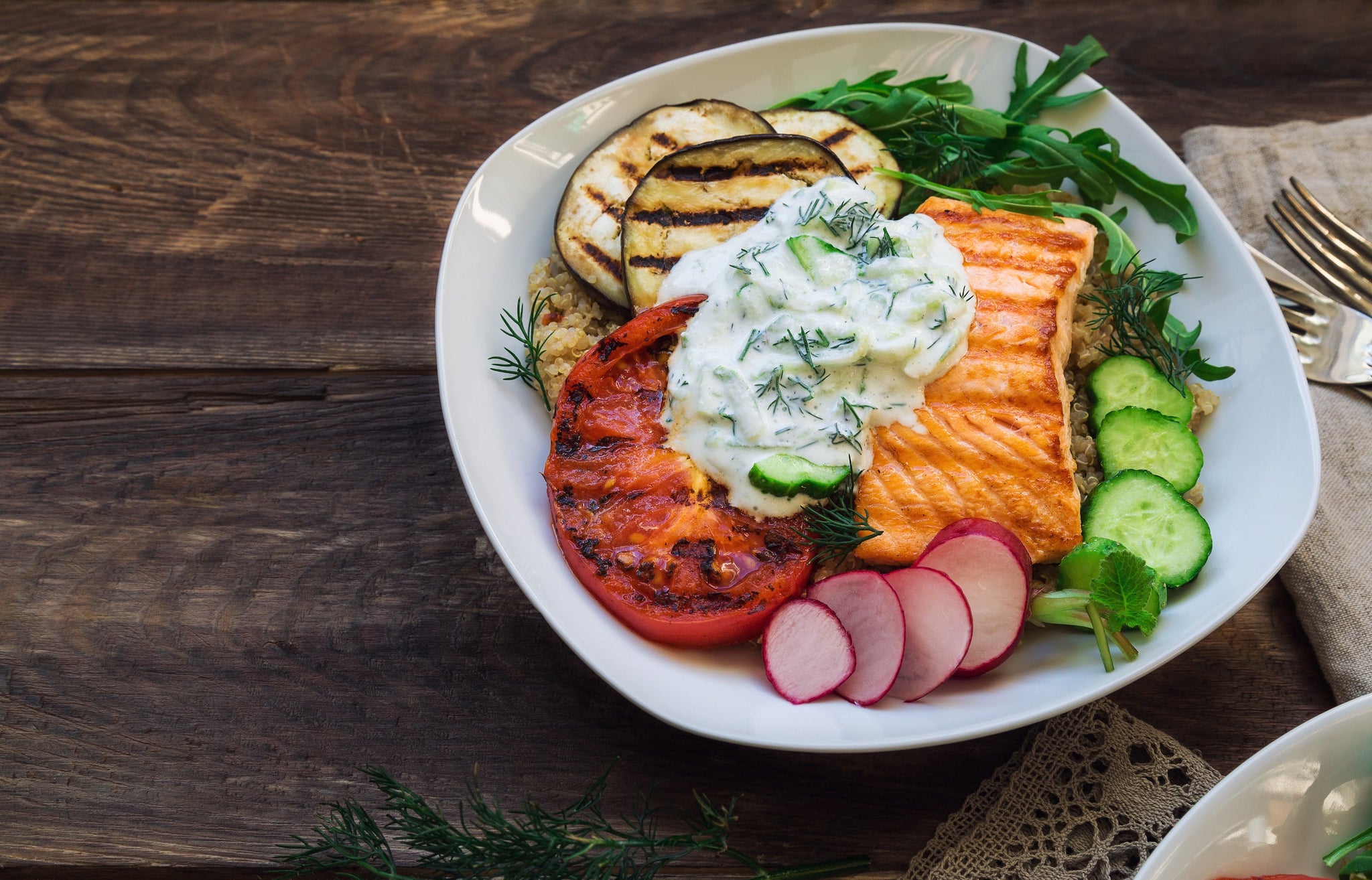 Bowl with grilled salmon, quinoa, vegetables, and tzatziki on a rustic wooden table.