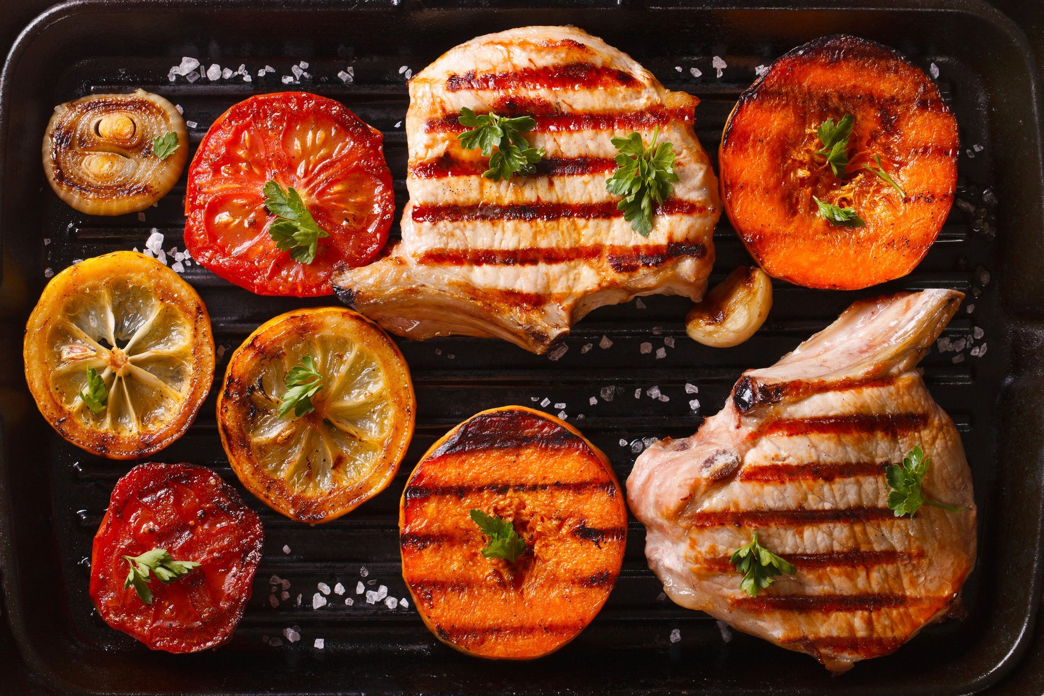 Grilled pork chops with charred tomatoes, lemon slices, onions and garnished vegetables on a grill pan.