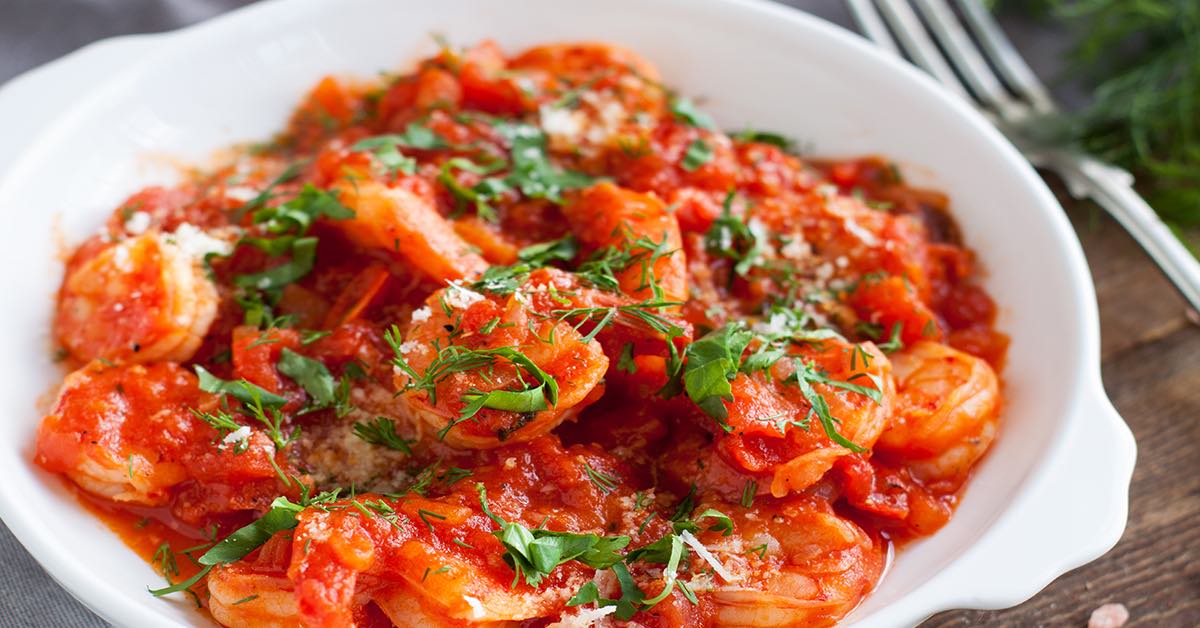 Shrimp cooked in a rich tomato sauce, topped with chopped fresh herbs and served in a white dish.