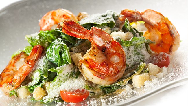 Grilled shrimp served over a Caesar-style salad with lettuce, tomatoes, croutons, and grated cheese.