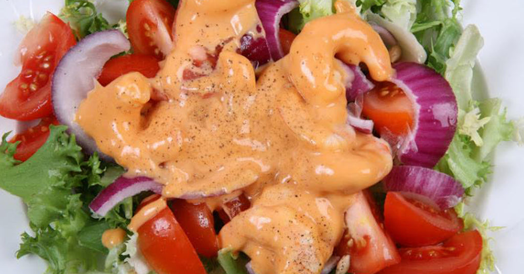 Fresh salad with tomatoes, onions, and greens topped with a creamy orange dressing.