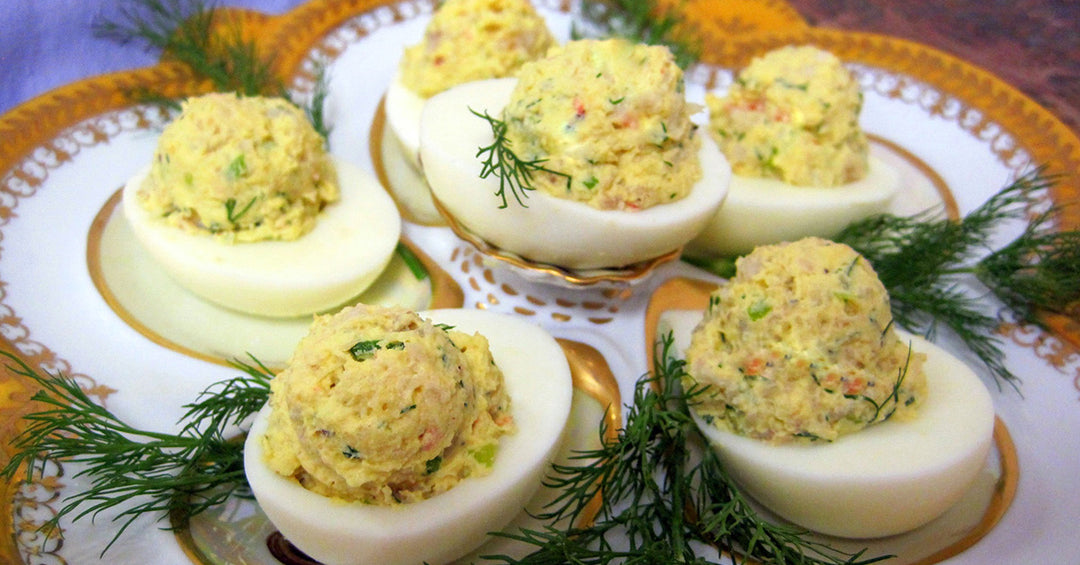 Deviled eggs filled with a herbed, creamy yolk mixture, garnished with fresh dill on a decorative plate.