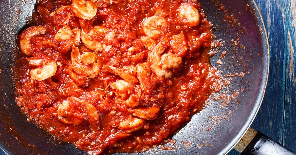 Shrimp simmering in a thick, chunky tomato sauce in a pan.