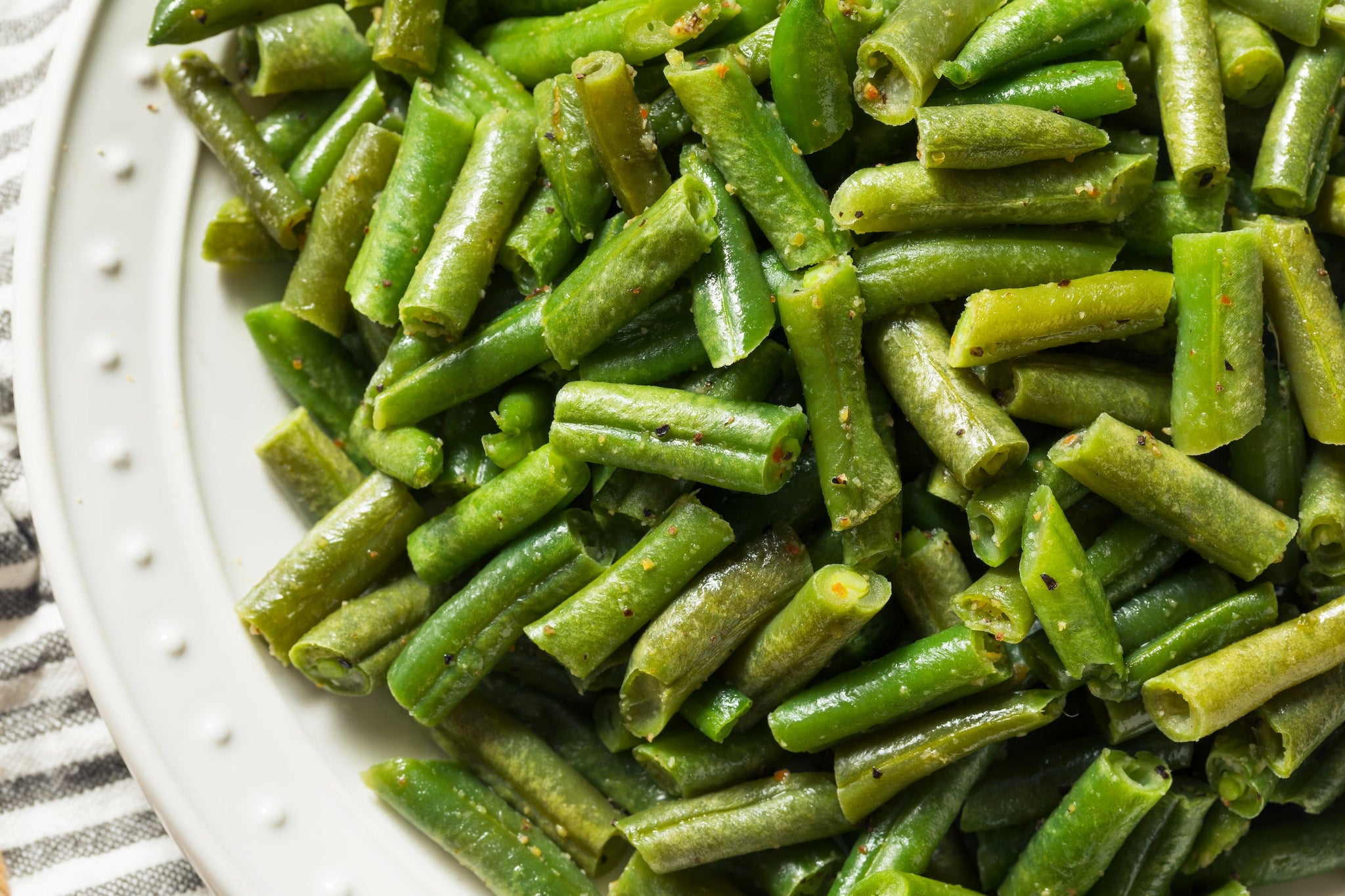 Close-up of cooked green beans seasoned lightly and served on a white plate.