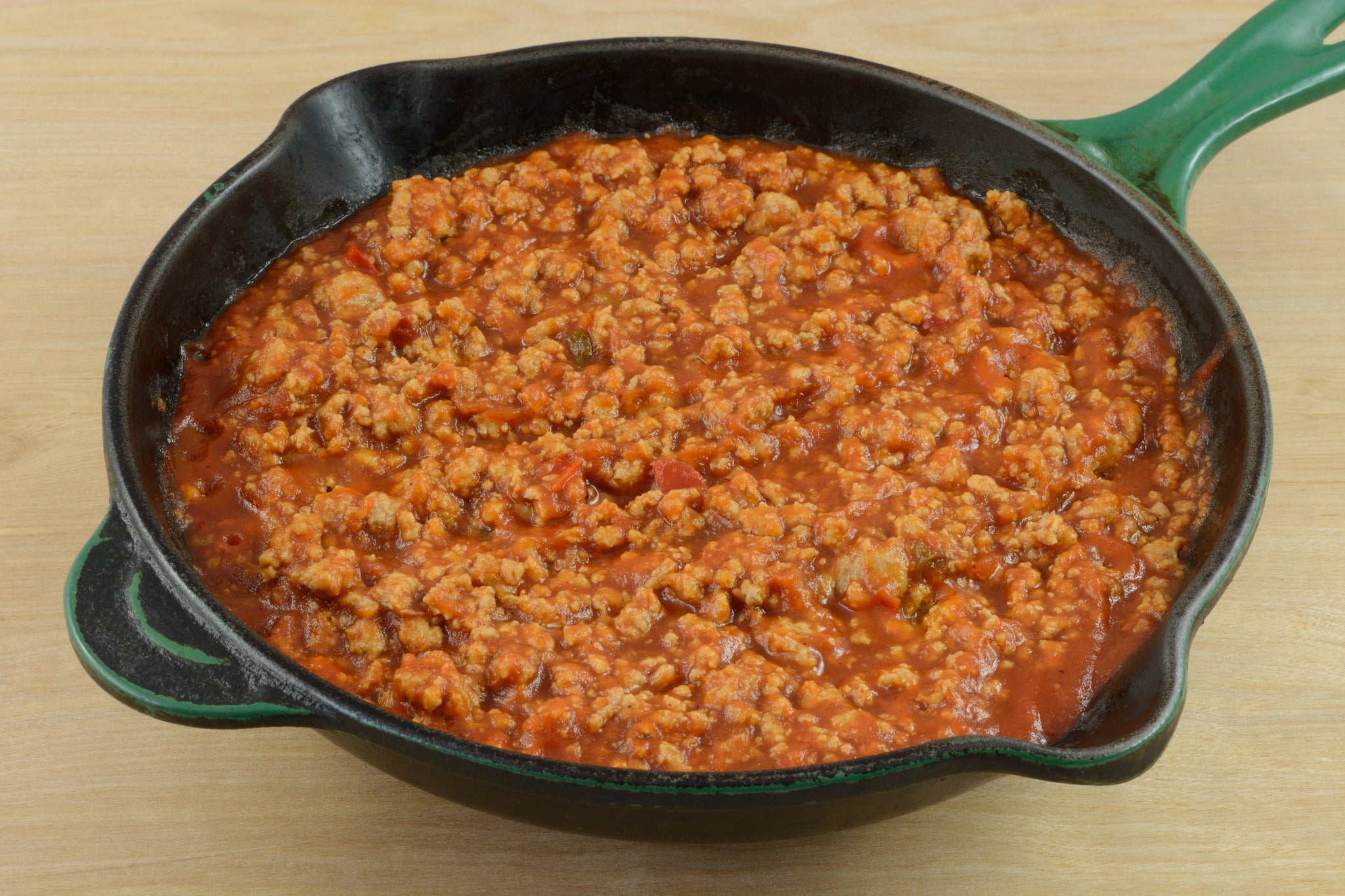 Skillet filled with thick, chunky tomato meat sauce on a wooden surface.