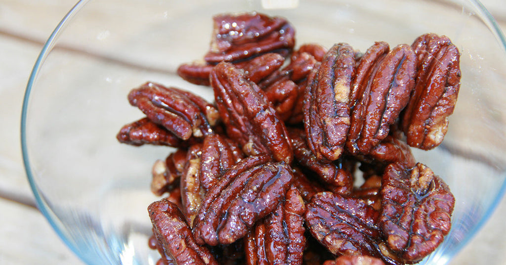 Close-up of glazed pecans piled in a glass bowl.