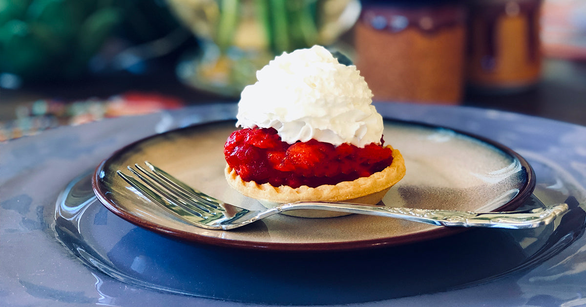 Small strawberry tart topped with whipped cream on a plate with a fork.