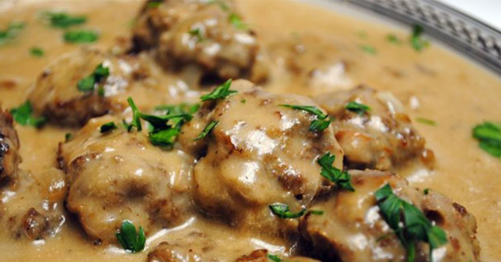 Meatballs covered in creamy brown gravy, garnished with chopped fresh herbs.