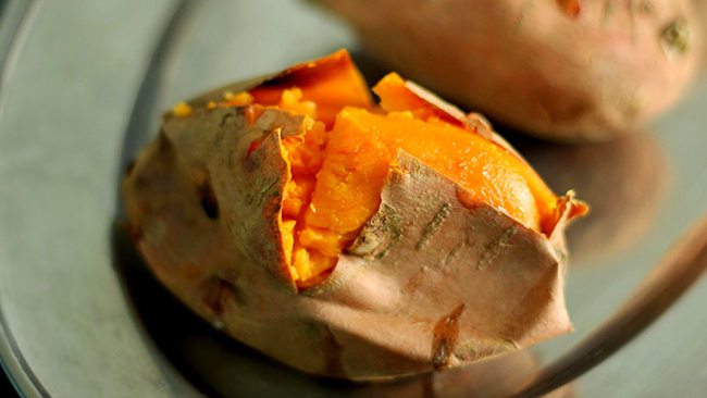 Baked sweet potato with its skin split open to reveal the soft orange flesh inside.
