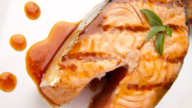 Grilled salmon steak topped with glaze and garnished with fresh basil on a white plate.
