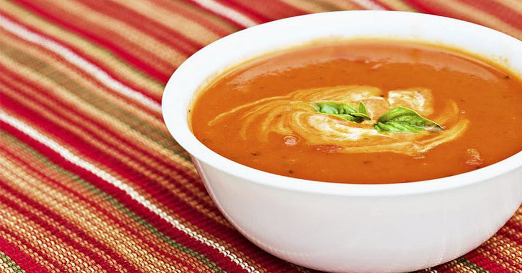 Bowl of creamy tomato soup with a swirl of cream and basil garnish on a red striped cloth.