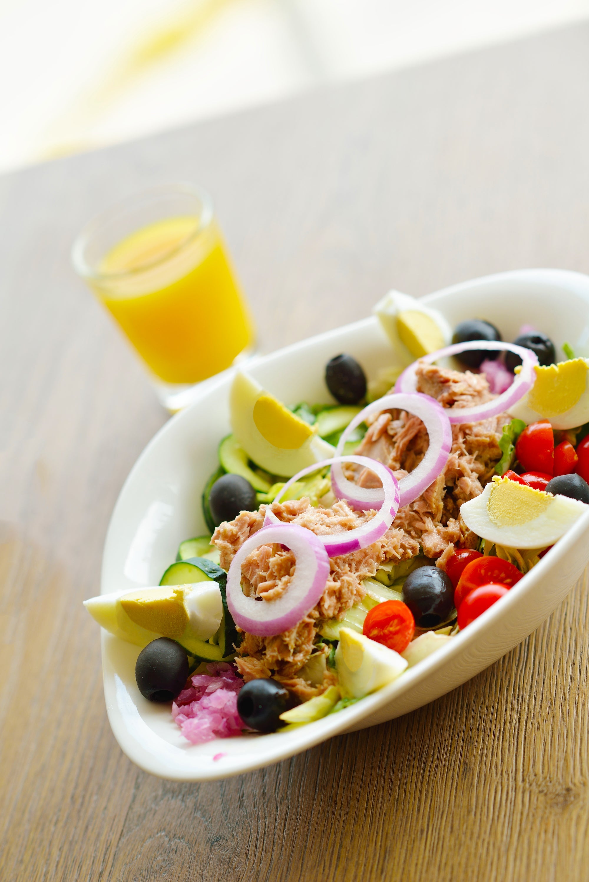 Fresh tuna salad with eggs, olives, cucumbers, tomatoes, and red onion, served with a glass of orange juice.