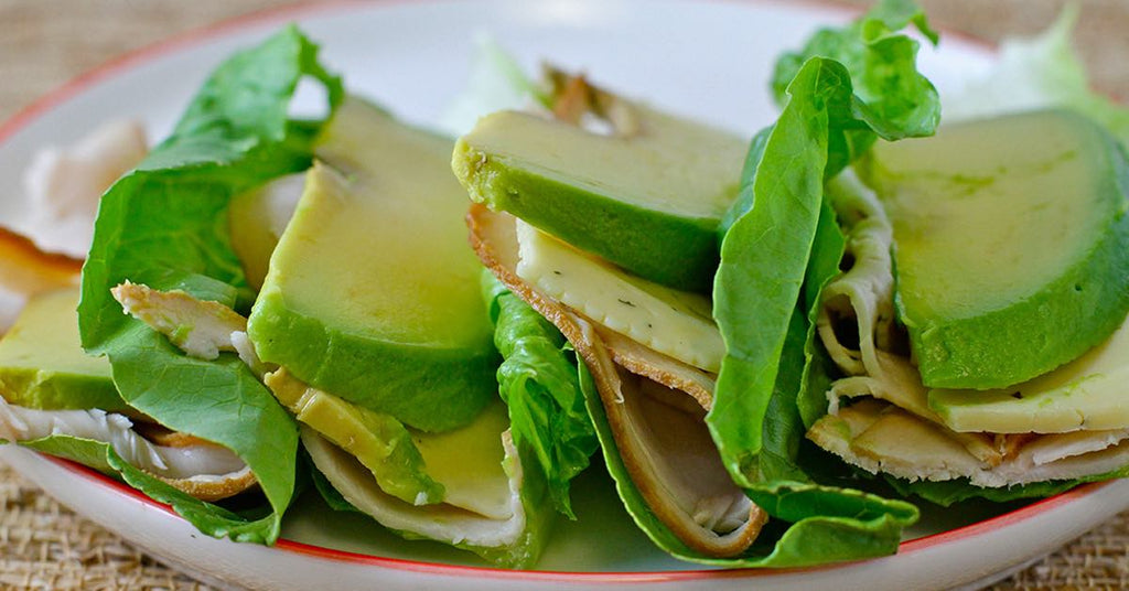 Lettuce wraps filled with sliced turkey, cheese, and avocado on a plate.