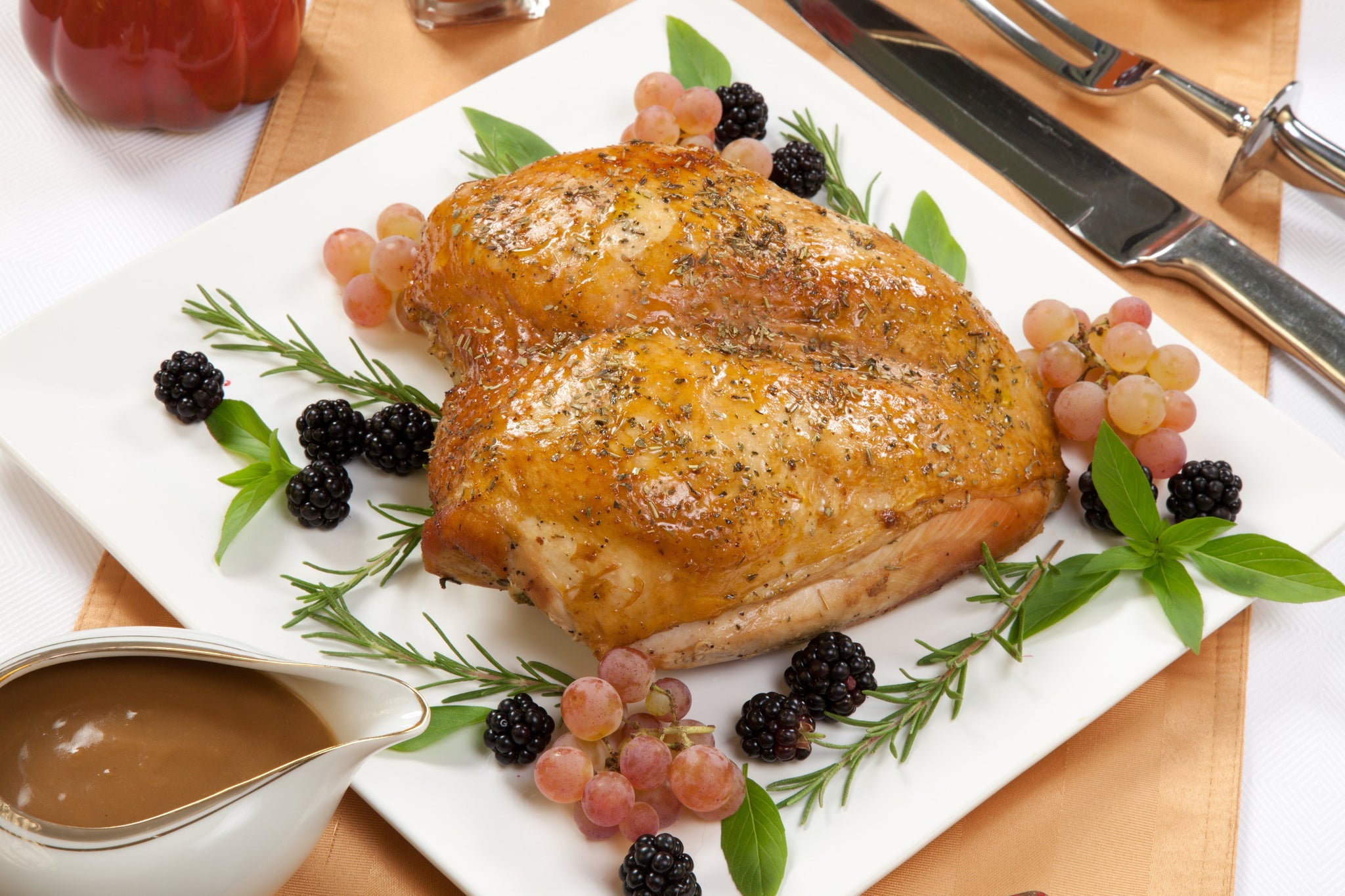 Roasted turkey breast on a white platter garnished with herbs, blackberries, grapes, and served with gravy.