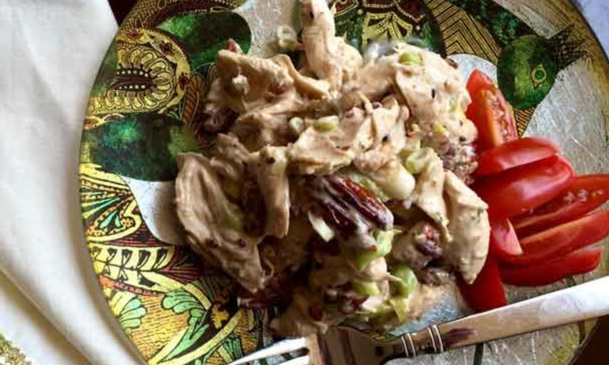 late of creamy chicken salad with pecans and green onions, served with sliced tomatoes and a fork.