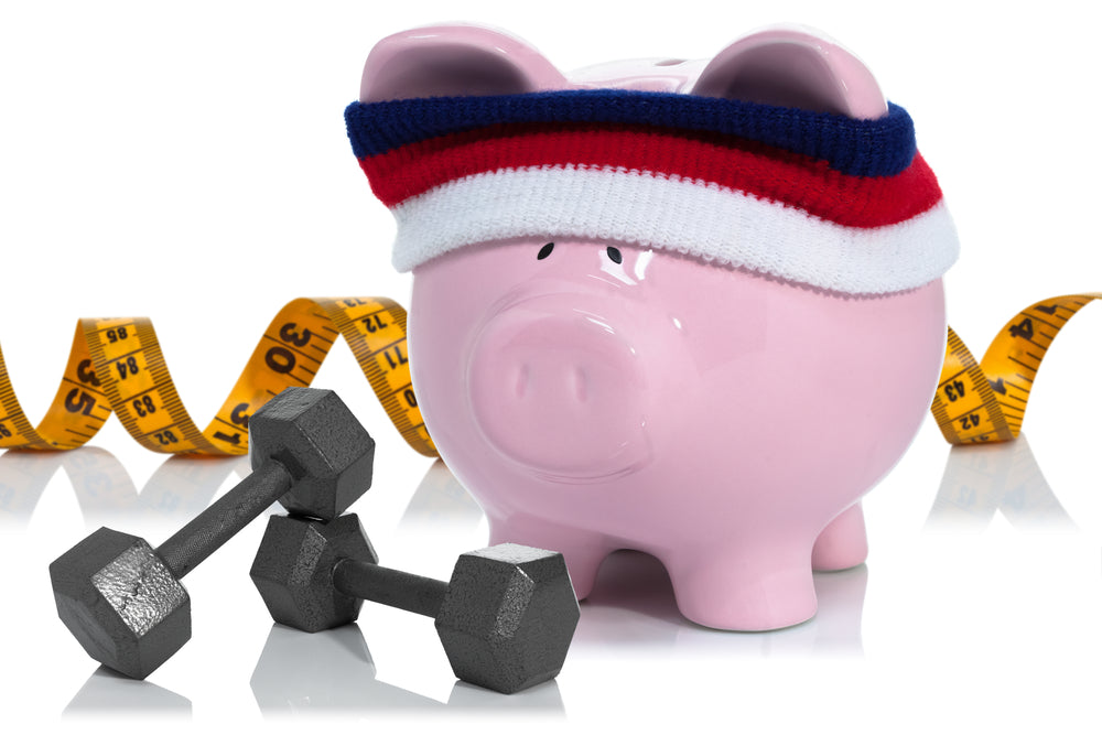 A pink piggy bank wearing a headband sits next to two small dumbbells and a measuring tape, symbolizing the concept of healthy eating on a budget while promoting fitness and financial wellness.