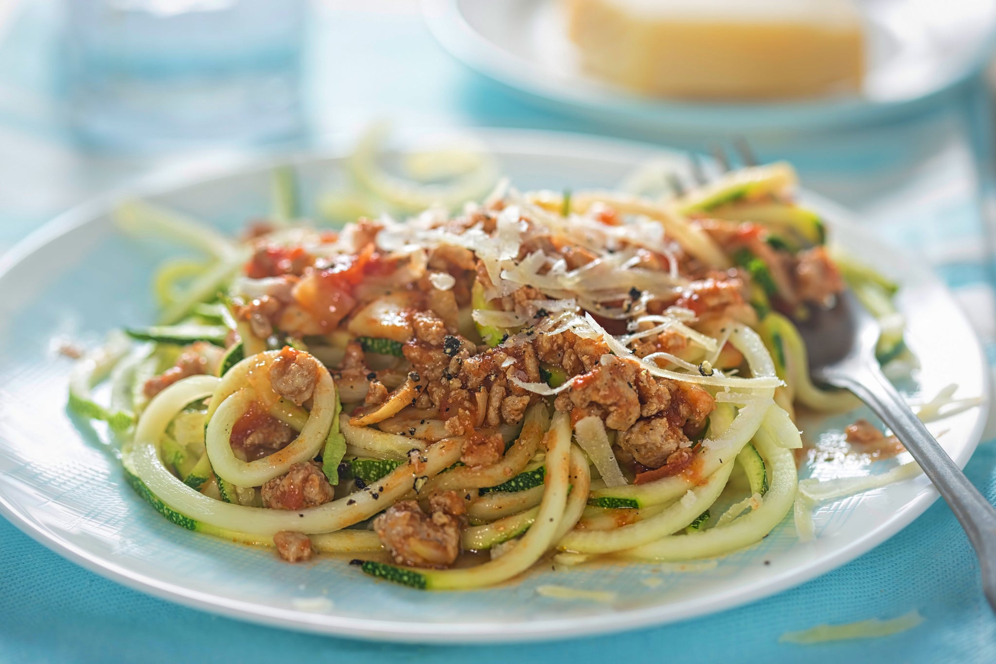 Zucchini noodles topped with minced meat in tomato sauce and grated cheese on a white plate.