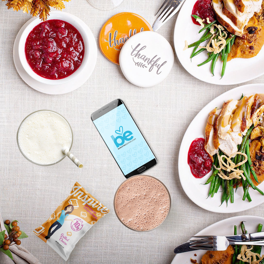Thanksgiving-style table with turkey plates, cranberry sauce, drinks, mini pumpkins, and a phone on a beige tablecloth.